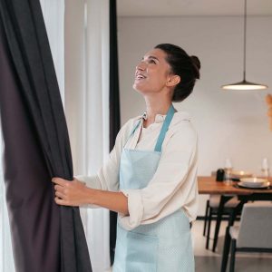 Young woman standing near the widnow and fixing the curtains